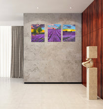 Load image into Gallery viewer, Room mock-up of a cream and red wall and the three lavender paintings together above a seat. Image shows Lengths of lavender stretch out in front up a hill towards tall poplar trees with a pink sunlit sky above; far away trees in silhouette with the orange sunset; the red roof cottage amid the copse of trees and below a moody sky.