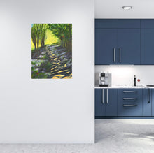 Load image into Gallery viewer, A tree lined path showing the sun peeping through the trees, leaving a shadowy light on the ground.  Bright sunlight and crop filled trees can be seen in distance.  Room mock-up of the blue kitchen with the painting on a pale wall - making the bluebells pop in the painting.