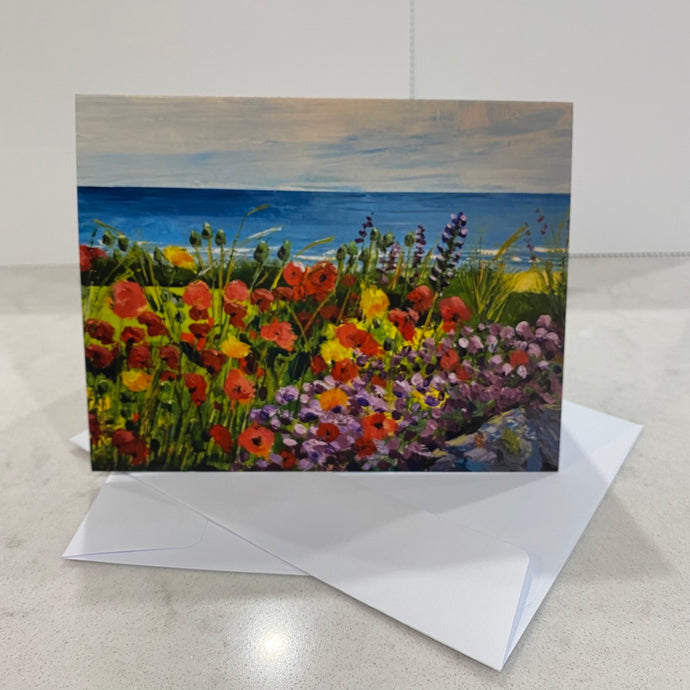 Seaside in background with wildflower garden full of poppies and lupins in foreground.  13.9 x10.7cm card. With envelope.  Blank inside