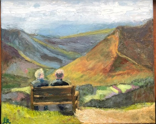 two men sitting on a bench overlooking a valley below full of colour and fields of crops 