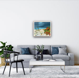 A seaside floral painting - Bettystown, Ireland.  A bed of daisies and red poker flowers are seen the the foreground with the sea and sky beyond.      A room mock-up of a sitting room with a sofa and the painting on the wall above,