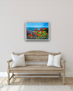 Image of the painting in a white frame in a hallway, over a cream wooden bench. 