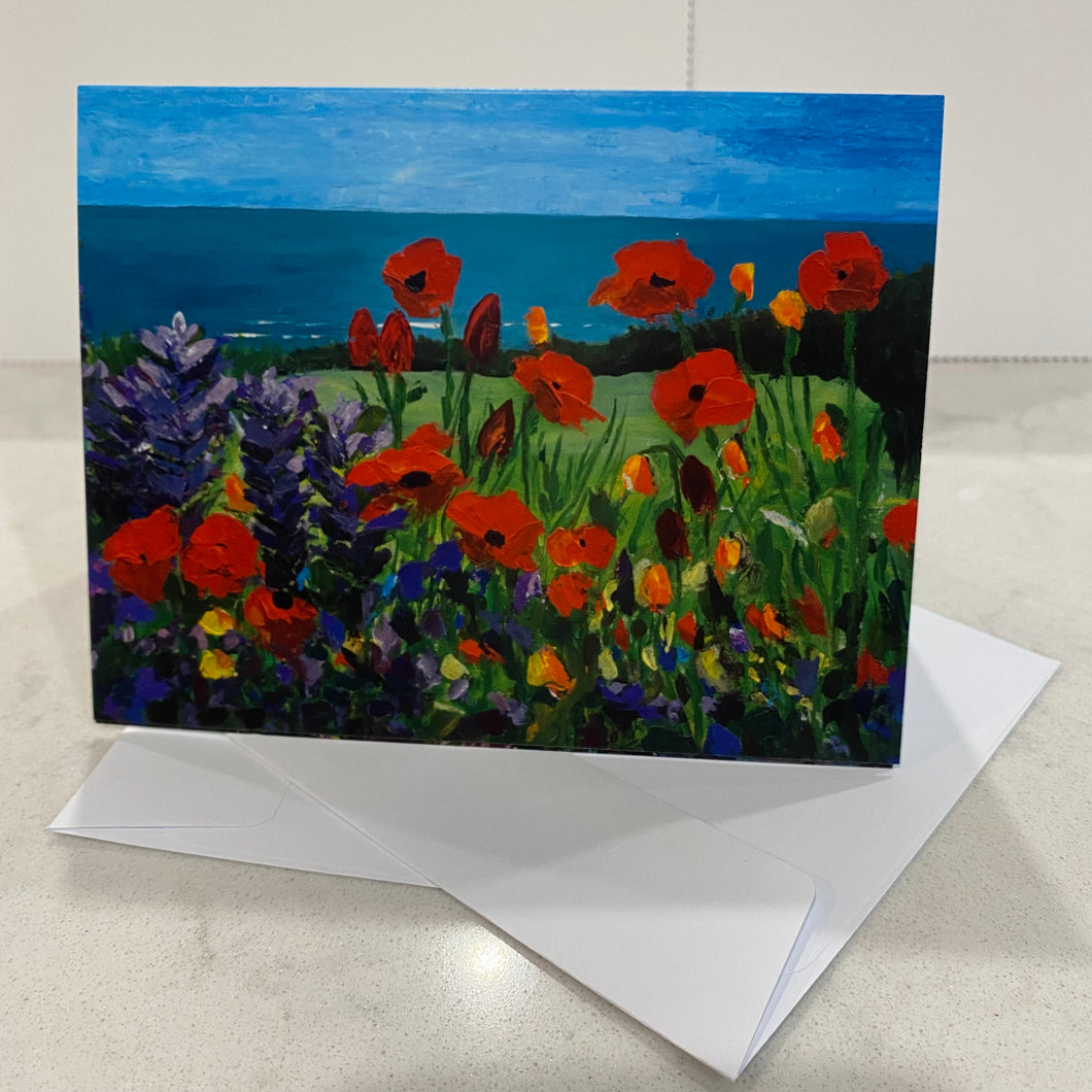 13.9 x10.7cm card with image of seaside in distance, poppies and other wildflowers in foreground. Blank inside.  Image from original painting