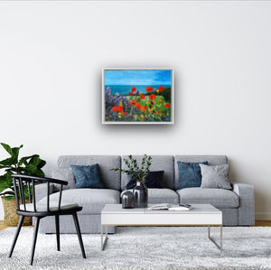 Room setting image of painting in white frame over a grey sofa in a comfortable sitting room  