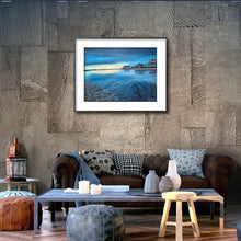 Load image into Gallery viewer, Room setting with the blue Nanny Cottage painting on the wall and blue brown cream accessories and sofa beneath in the room setting image.  Shown in a black frame with a white mount to show the drama of the colours.  Art gift. scenic, atmospheric. sunrise Ireland