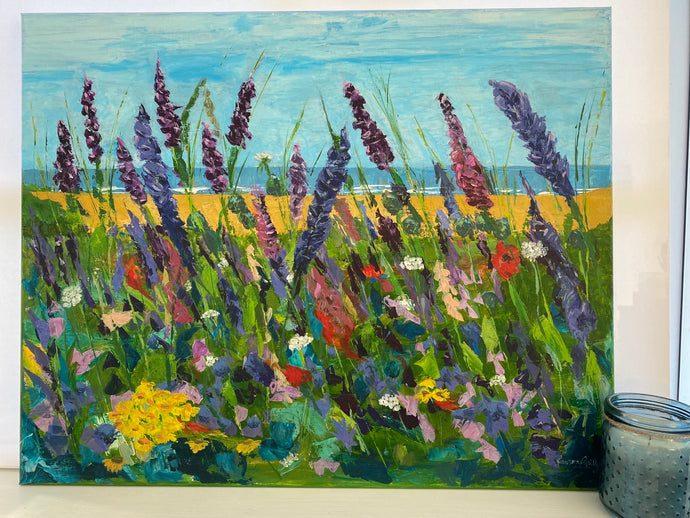 a beach beyond with a splash of wildflowers in the foreground  purples pinks yellow and blue red greens 
